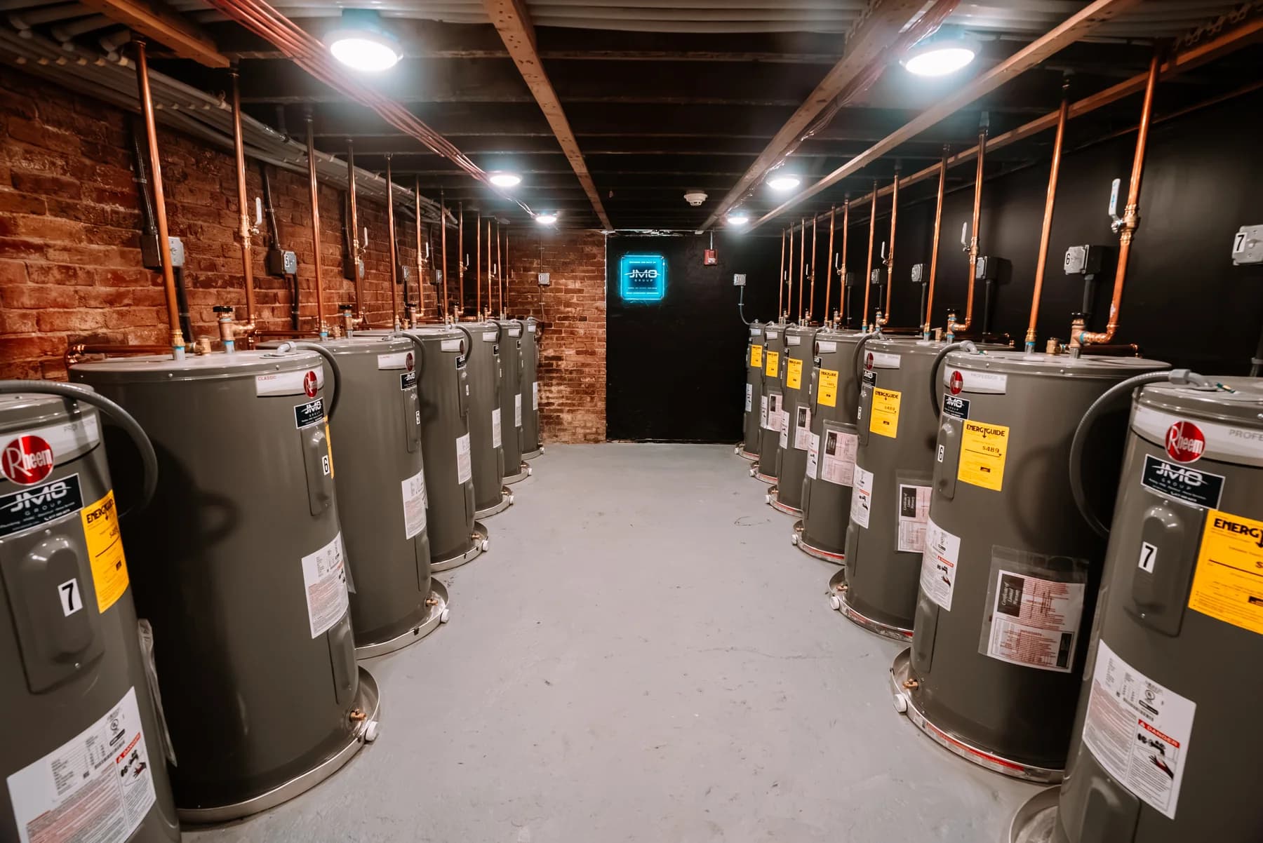 Water heaters and copper pipework in a mechanical room with JMO branding
